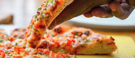 A hand holding a slice of pizza with visible toppings, placed on a yellow surface.