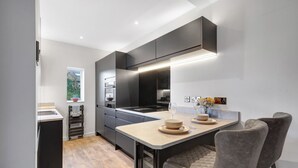 A modern kitchen with a central island, dark cabinetry, and a dining area with two chairs.