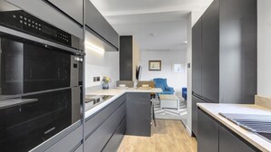 A modern kitchen with a built-in oven, a dining area with a blue chair, and a small seating area with a sofa.