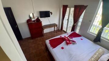 Quarto com uma cama, cômoda, televisão e janela com cortinas.
