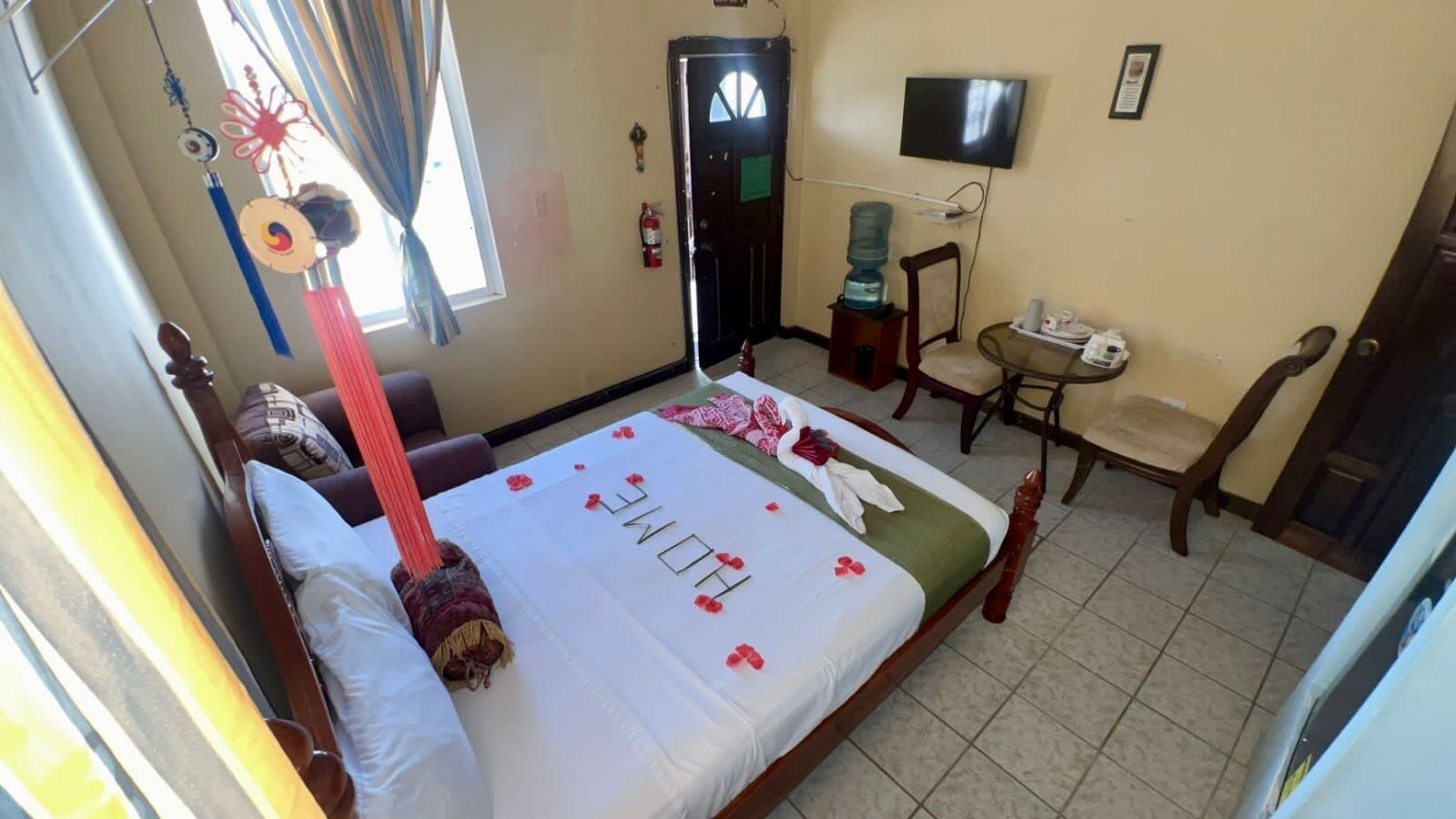 Habitación de hotel con cama, escritorio, silla, televisor y dispensador de agua.