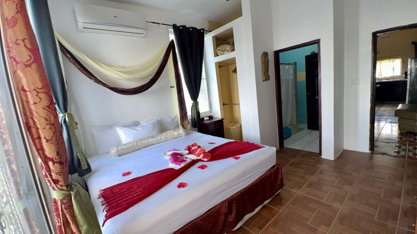 A hotel room with a bed, curtains, a window, and a door leading to another room.