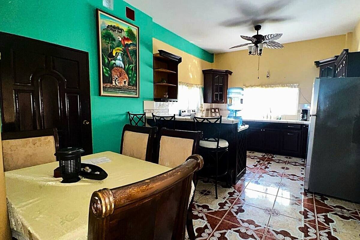 A kitchen with a dining table, chairs, a refrigerator, and a ceiling fan.