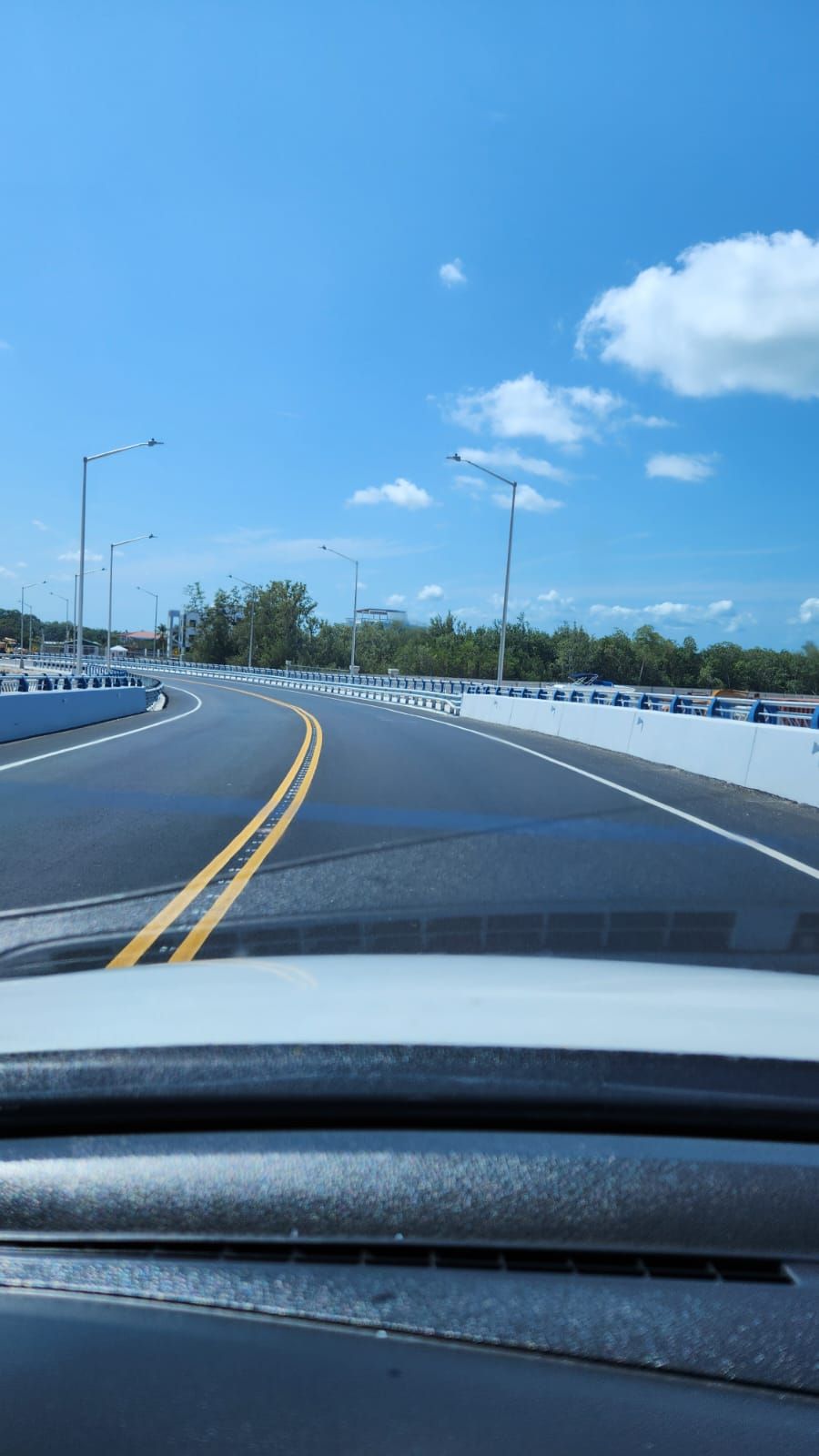 A clear road with a double yellow line, streetlights, and a guardrail.