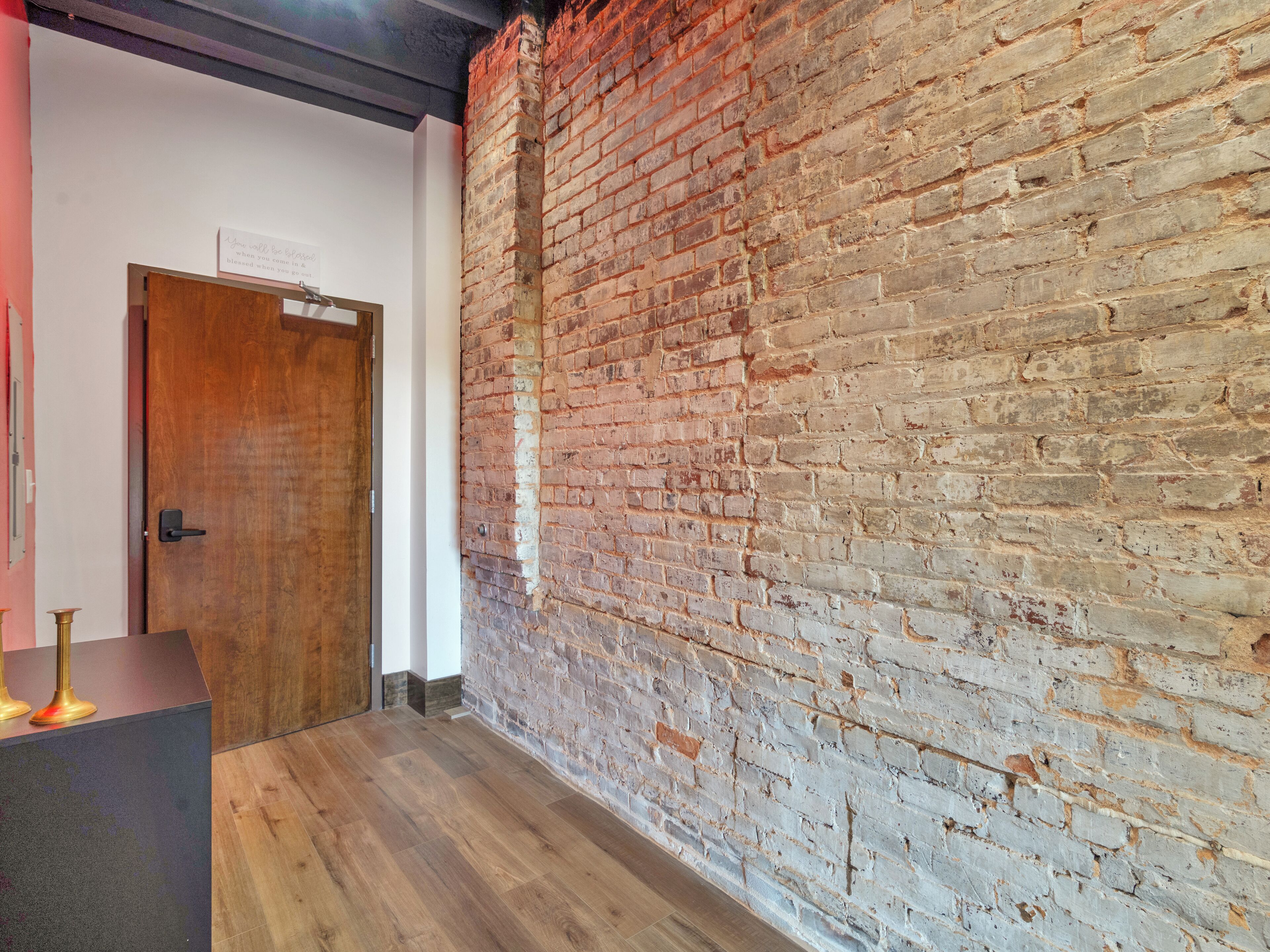 A hallway with a wooden floor, a brick wall, and a wooden door.