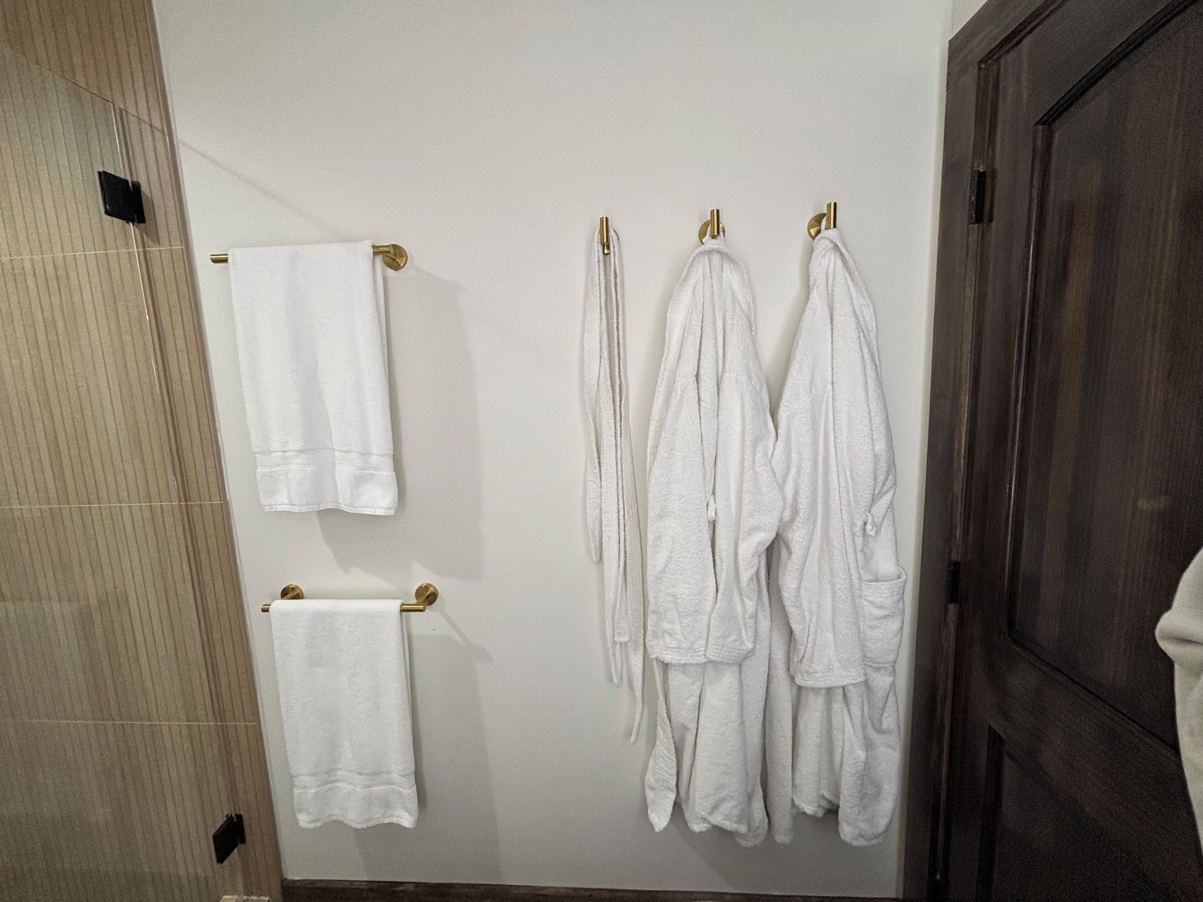 A bathroom with a wooden door, a towel rack with multiple white towels, and a tiled wall.