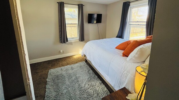 Een slaapkamer met een bed, een flatscreen televisie en een raam met gordijnen.