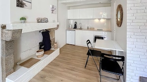 A modern kitchen with white cabinets, a stone fireplace, and a dining area with a table and chairs. - Charming newly renovated studio with terrace - pets allowed, free Wi-Fi (Granville)