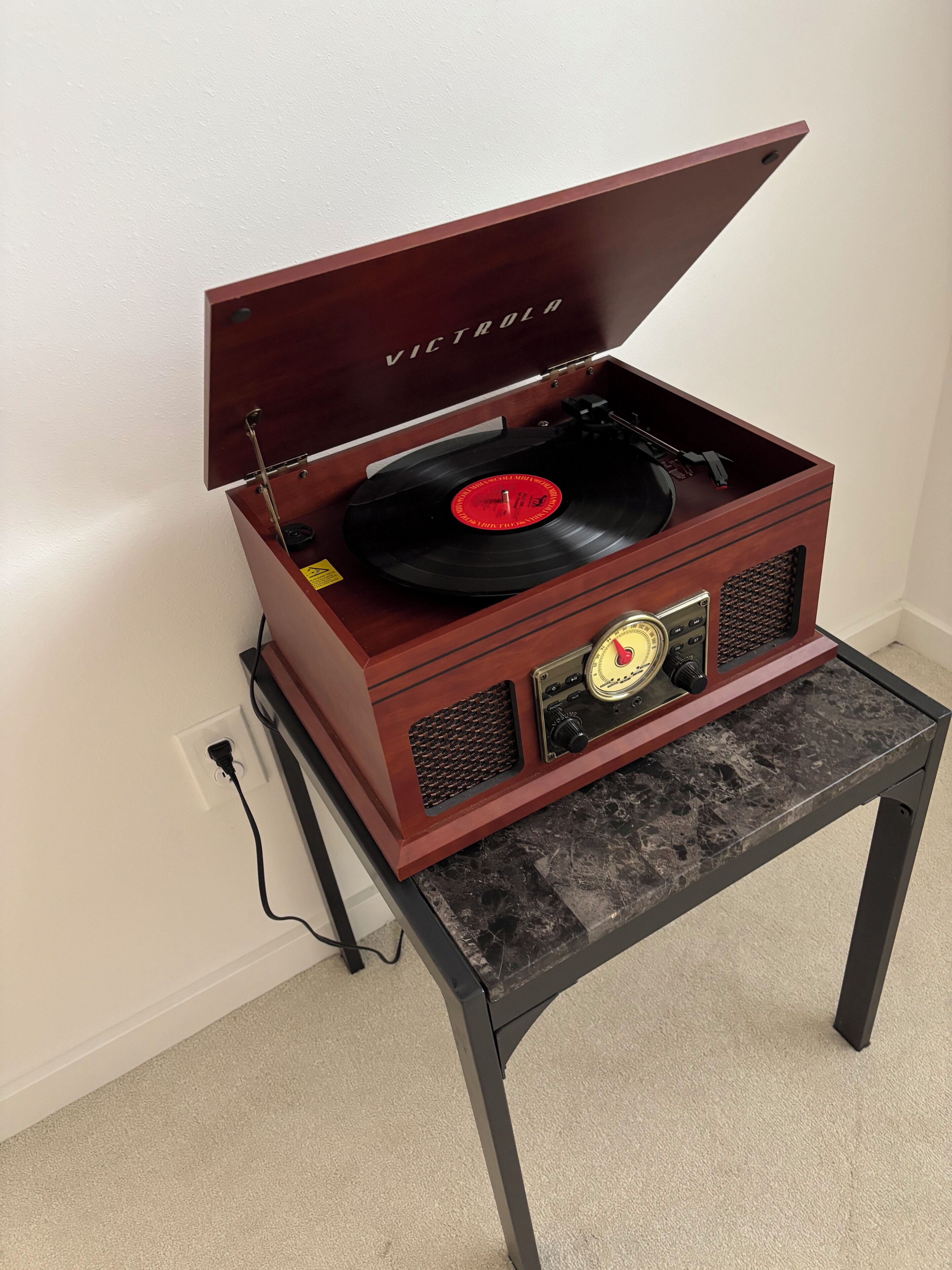 En grammofon av trä med en röd vinylskiva på ett bord av marmor.