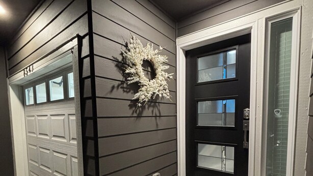 Une maison à l’extérieur d’un gris foncé, avec une porte d’entrée noire dotée d’un panneau de verre et une porte de garage.