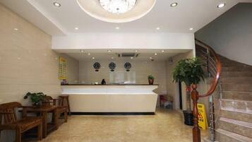 A hotel lobby with a reception desk, seating area, and a staircase.