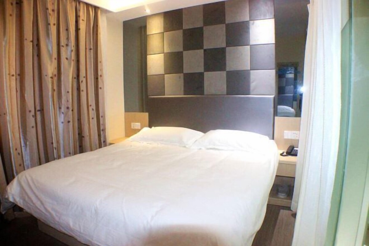 A hotel room with a bed, a headboard with a checkered pattern, a nightstand, and a curtain.