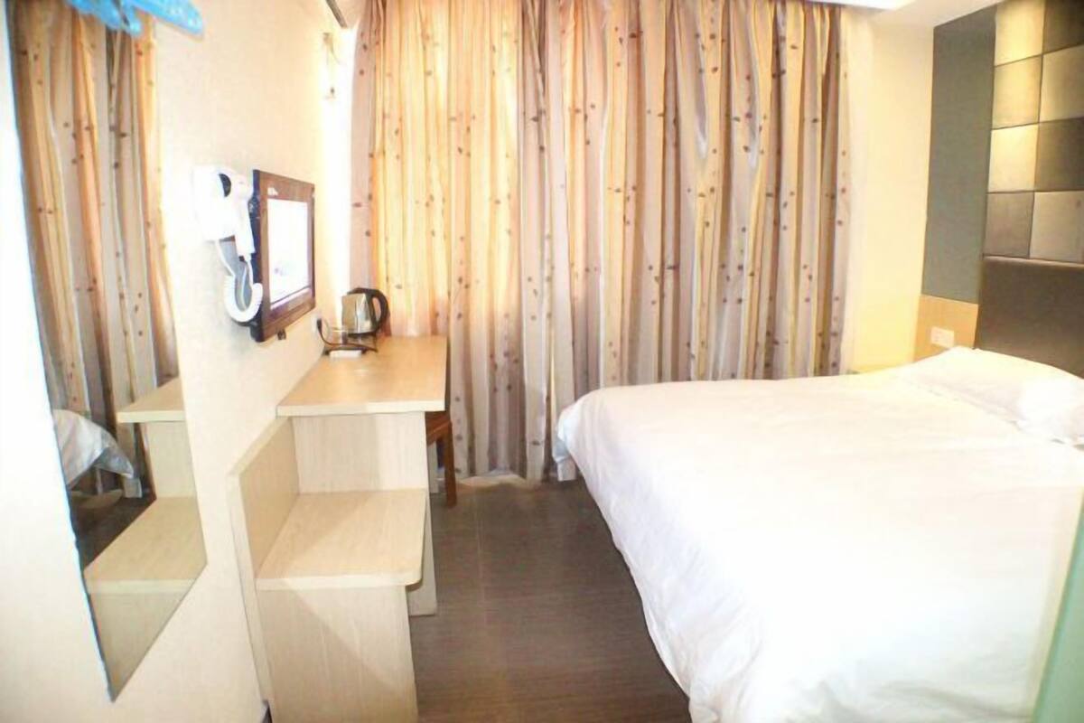 Una habitación de hotel con cama, escritorio, silla, cafetera y cortinas.