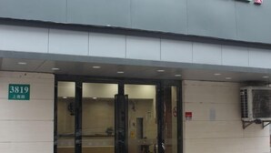 Entrada de hotel con puerta de vidrio, un letrero con el número 3819 y una unidad de aire acondicionado montada en la pared.