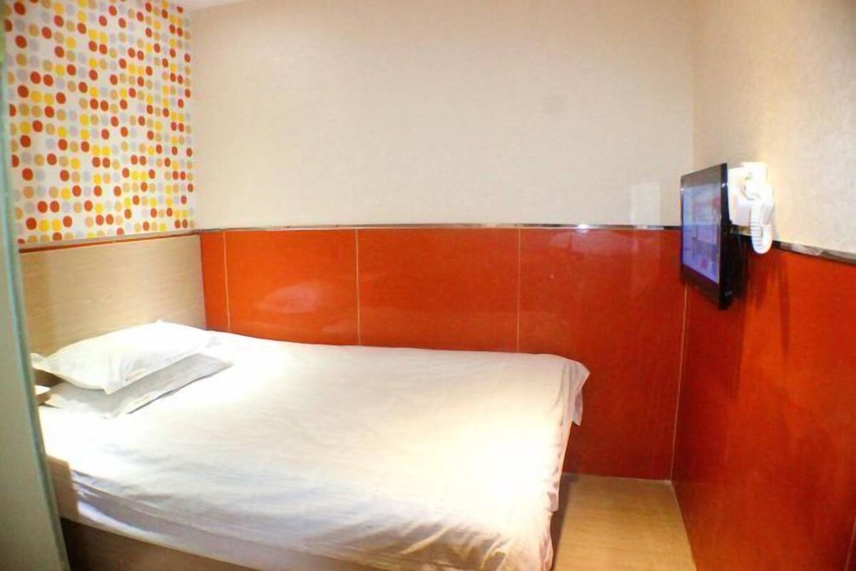 Una habitación pequeña con cama individual, una colcha blanca sencilla, un televisor montado en la pared y un teléfono.