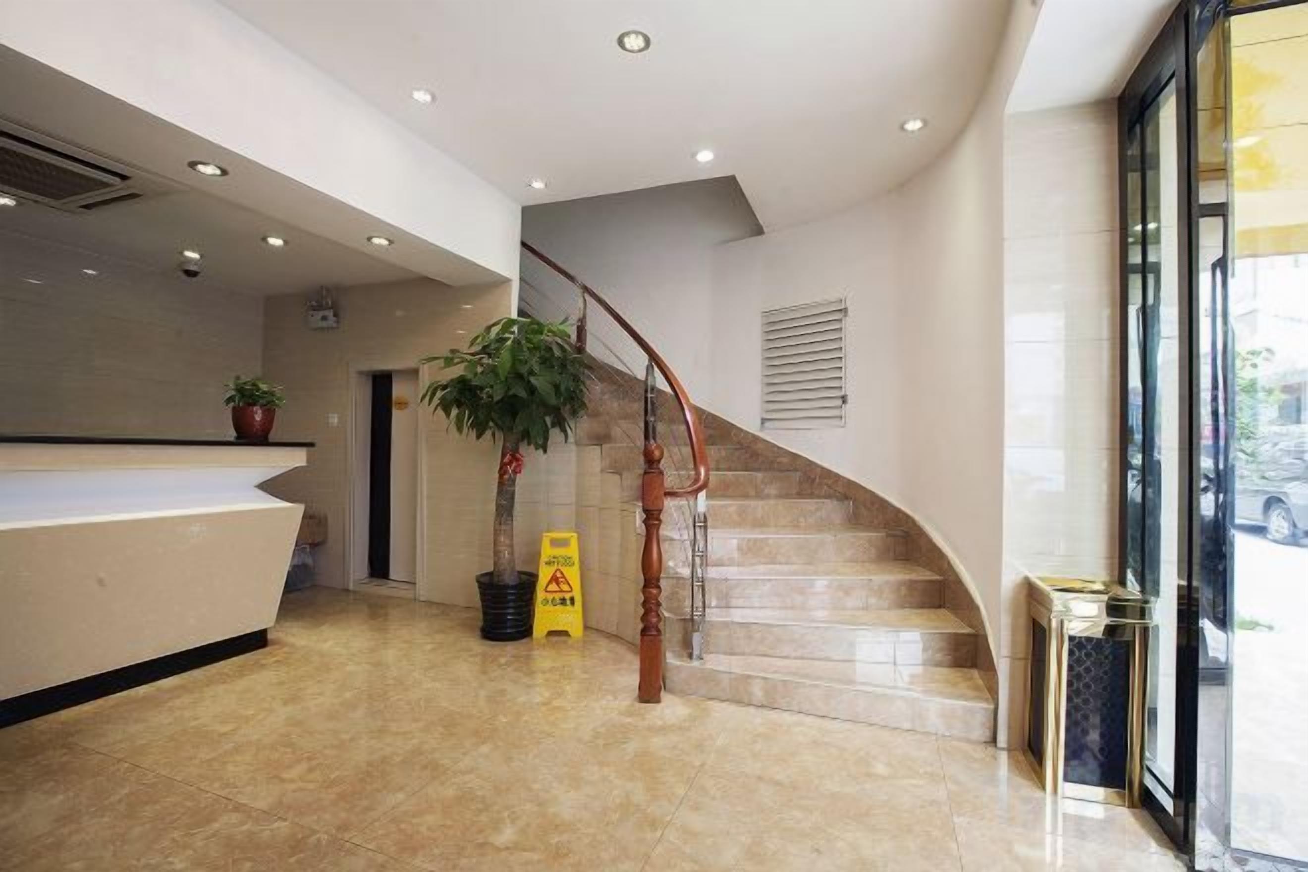 A hotel reception area with a reception desk, a staircase, and a potted plant.