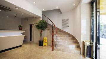 A hotel reception area with a reception desk, a staircase, and a potted plant.