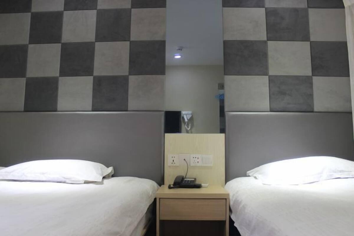 Habitación de hotel con dos camas, una mesita de noche pequeña con un teléfono y un espejo.
