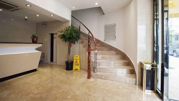 Un área de recepción con piso de mármol, mostrador de recepción, una escalera y una planta en maceta.