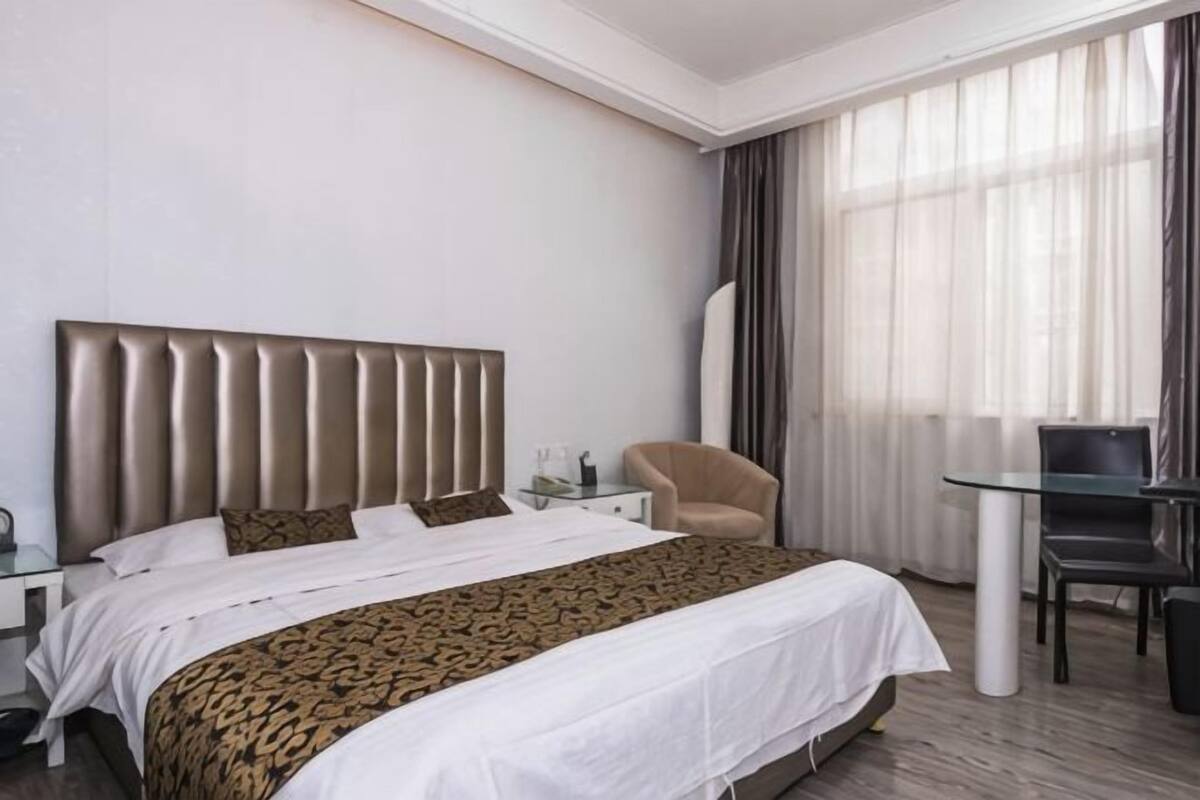 Ein Hotelzimmer mit einem großen Bett, einem Sessel, einem kleinen Tisch und einem großen Fenster mit Vorhängen.