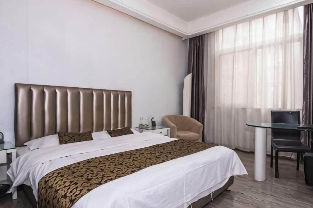 A hotel room with a large bed, a chair, a small table, and a large window with curtains.