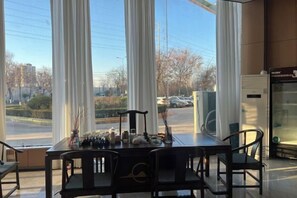 A dining area with a table and chairs, large windows with curtains, and a view of the street outside. - Mingjun Fashion Hotel (Shangqiu)