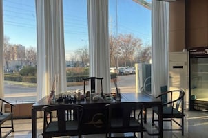 Un comedor con mesa y sillas, ventanas amplias con cortinas y vista a la calle.