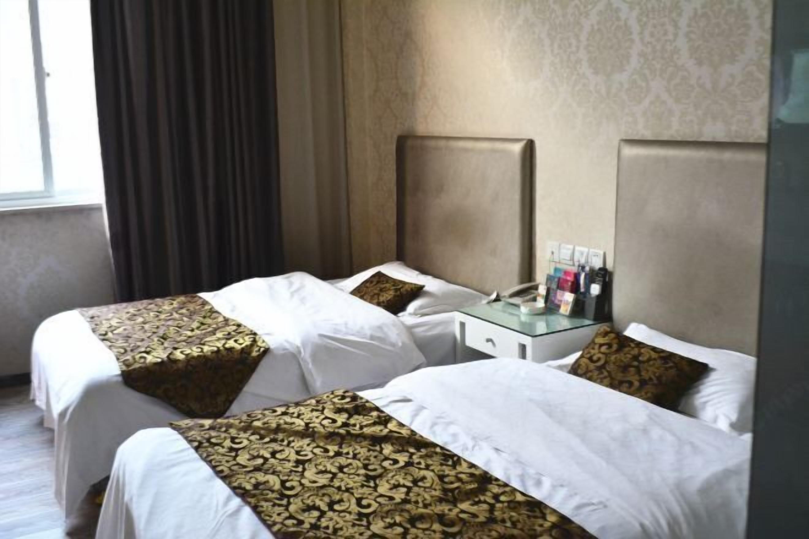 Quarto de hotel com duas camas, uma mesa de cabeceira e uma janela com cortinas.