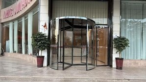 A revolving door with glass panels, potted plants on either side, and a building entrance with a sign above. - Mingjun Fashion Hotel (Shangqiu)