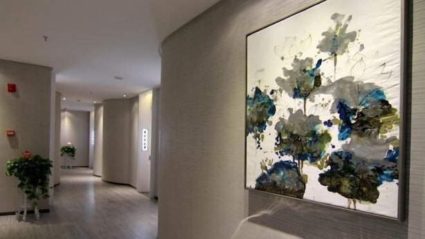 A hallway with a large abstract painting on the wall, potted plants, and a modern interior design. - Mingjun Fashion Hotel (Shangqiu)
