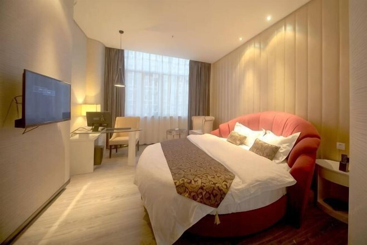 Ein Hotelzimmer mit einem großen Bett, einem Schreibtisch mit Stuhl, einem Fernseher und einem Fenster mit Vorhängen.