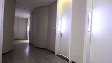 A corridor with doors on the right, a wooden floor, and recessed lighting.