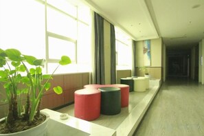 A hotel lobby with a reception desk, a potted plant, and a row of red and black stools. - Mingjun Fashion Hotel (Shangqiu)