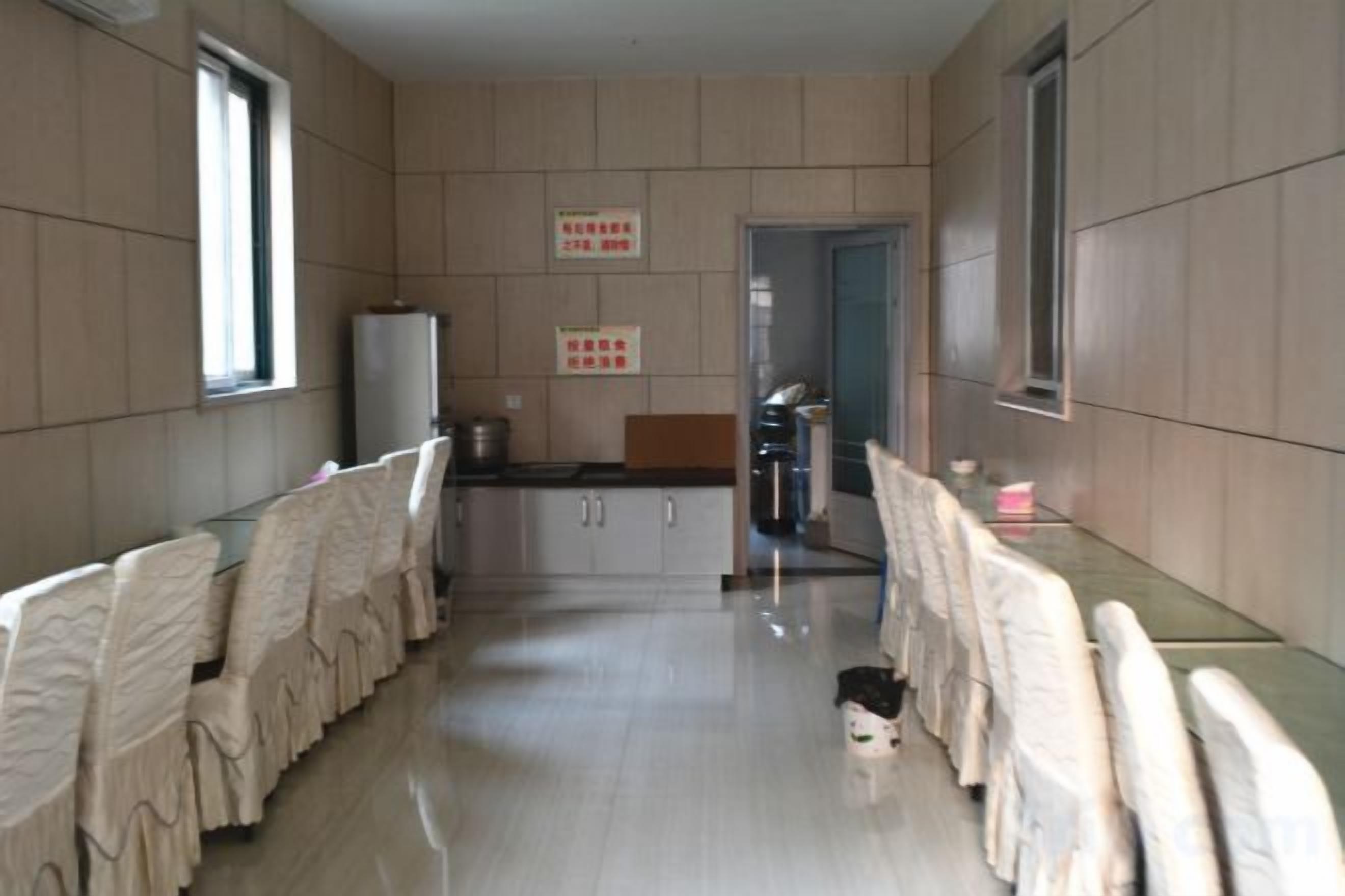A corridor with a long table, chairs, and a refrigerator.