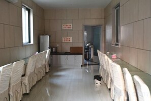 Ein Korridor mit einem langen Tisch, Stühlen und einem Kühlschrank.