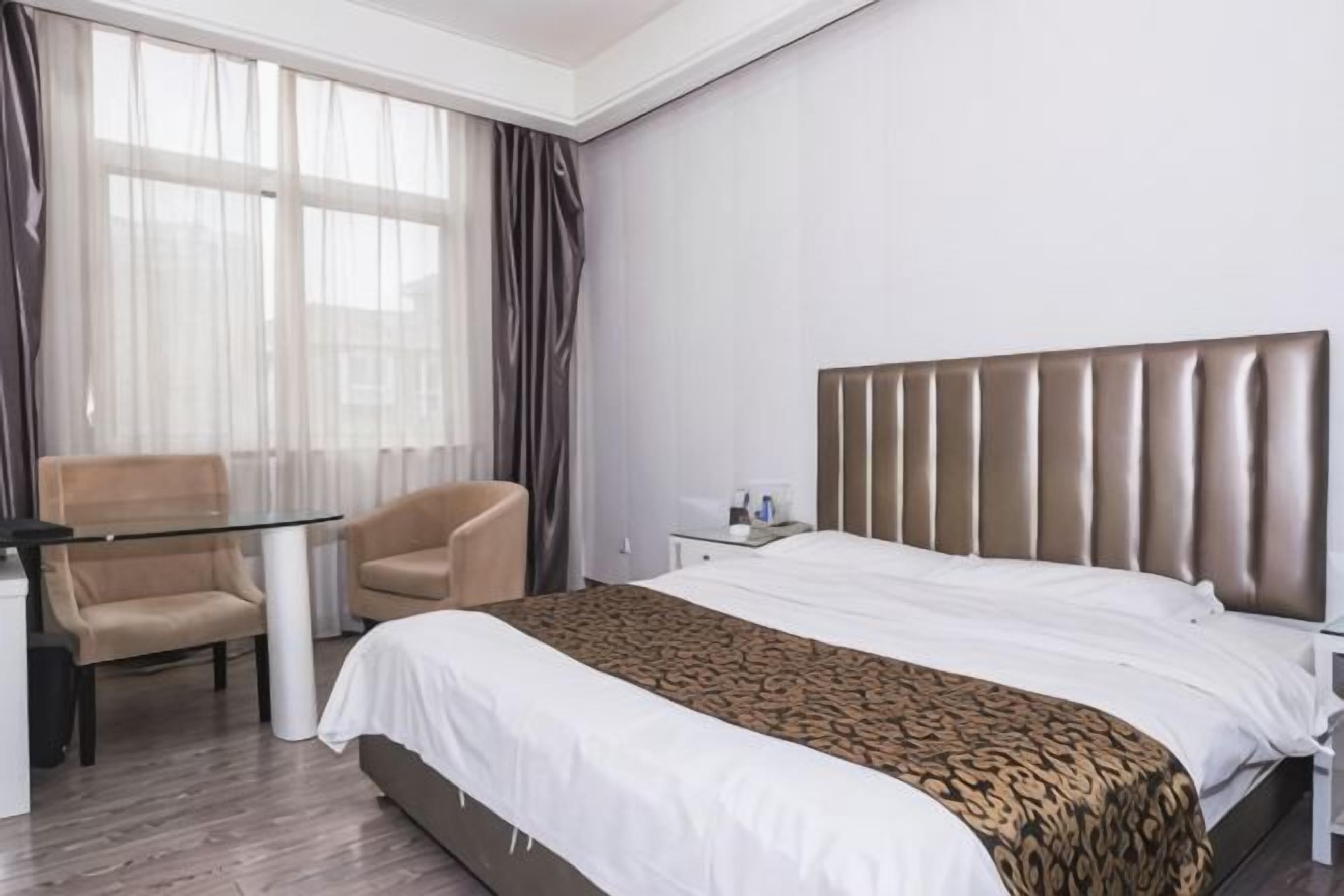 A hotel room with a bed, a desk, a chair, and a window with curtains.
