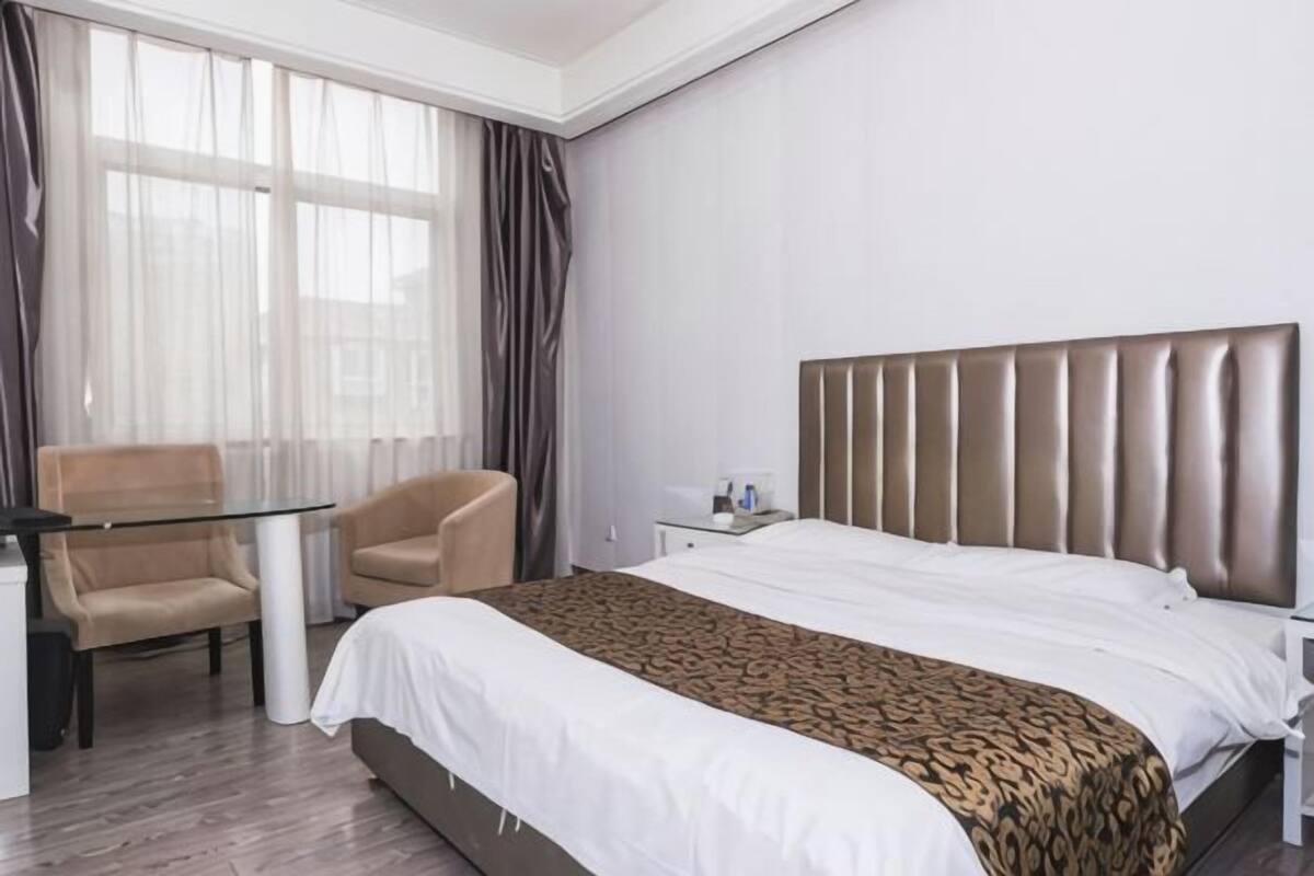 Ein Hotelzimmer mit Bett, Schreibtisch, Stuhl und einem fenster mit Vorhängen.