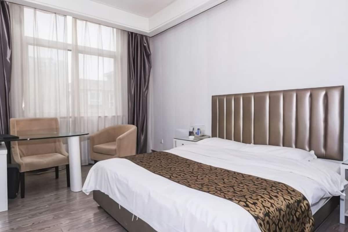 A hotel room with a bed, a desk, a chair, and a window with curtains.