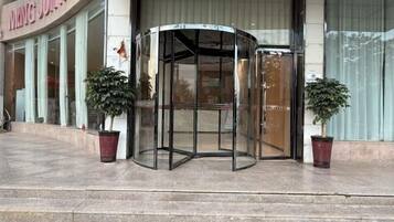 Une porte tournante avec des panneaux de verre, un pot de fleurs à gauche et un pot de fleurs à droite.