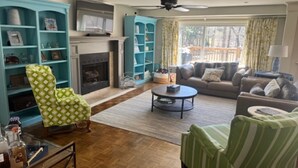 A living room with a fireplace, teal shelving, and a green armchair. - 5 Bedroom House (Greensboro)