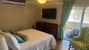 A bedroom with a bed, dresser, TV, and a chair by a sliding glass door. - 5 Bedroom House (Greensboro)