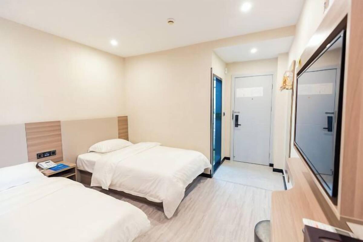 Habitación de hotel con dos camas, un escritorio, un televisor y una puerta que da a otra habitación.