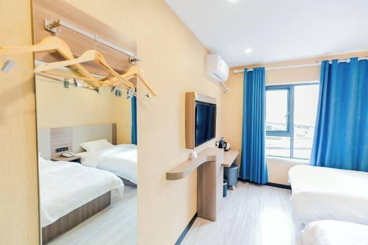 Habitación de hotel con dos camas, televisión, escritorio y ventana con cortinas azules.
