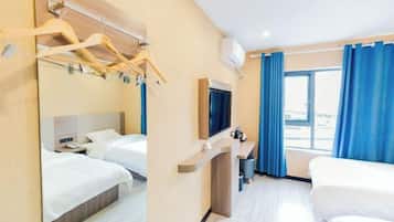 A hotel room with two beds, a TV, a desk, and a window with blue curtains.