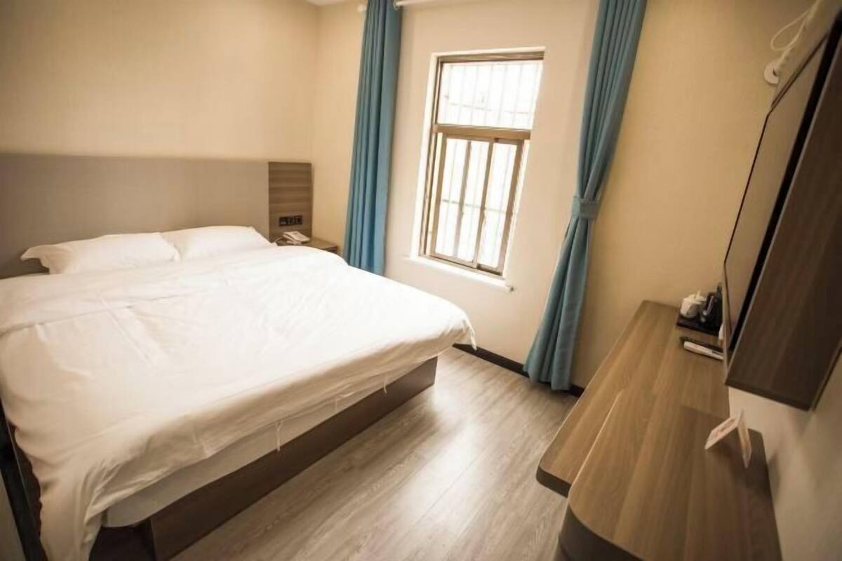 Habitación de hotel con cama, mesita de noche, ventana con cortinas y suelo de madera.
