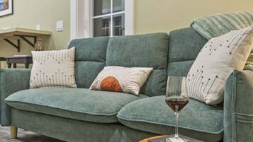 A green sofa with patterned pillows, a glass of red wine, and a small round table with a coaster.