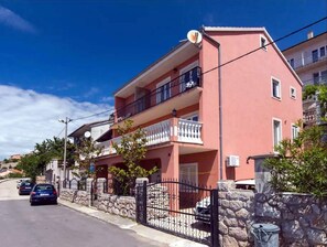 Stunning two-story residence with a balcony and satellite dish on the roof, set behind a stone wall.