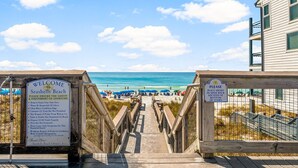 Une promenade en bois mène à une plage, et un panneau d’information se trouve à l’entrée.