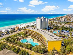 A resort with a large pool, beachfront view, and a tall hotel building.