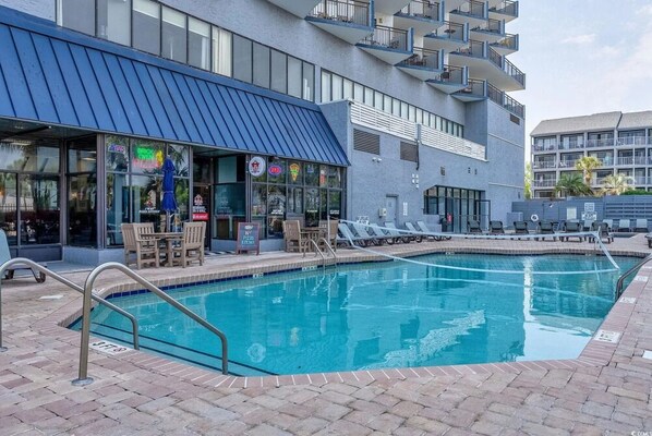 A pool area with lounge chairs and a restaurant with outdoor seating.